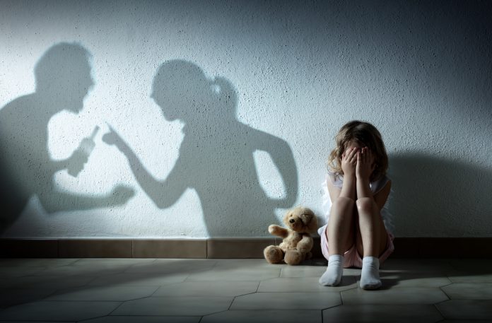In image of a small girl crying with shadows of parents arguing on the wall behind