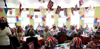 People celebrating the Queen's Platinum Jubilee, wearing hats and with bunting on the ceiling