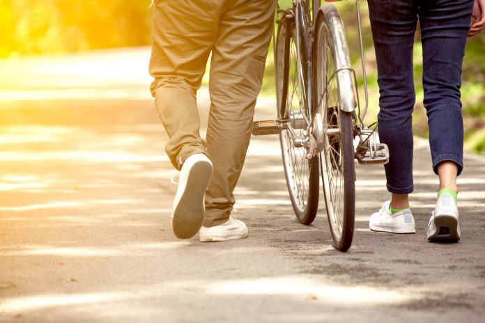 Back view of a male and female from behind walking, whilst one of them pushes a bicycle