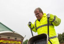 Councillor Steve Reade empties a wheelbarrow of tarmac on to a road