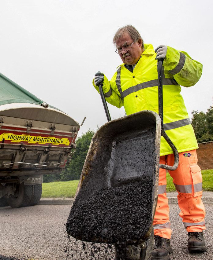 Councillor Steve Reade empties a wheelbarrow of tarmac on to a road