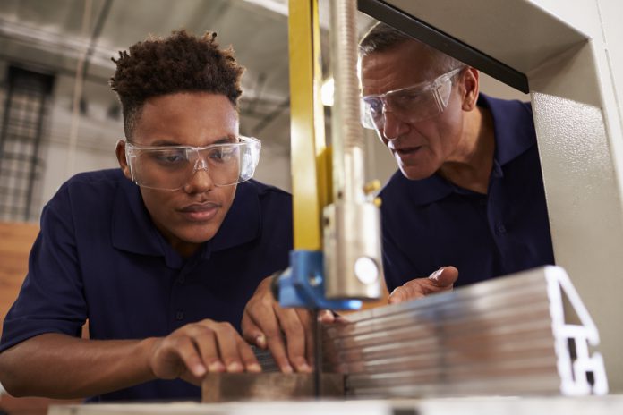 Carpenter training an apprentice to use mechanized saw