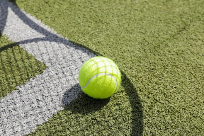 Shadow of a tennis racket on a grass tennis court with white lines and a tennis ball