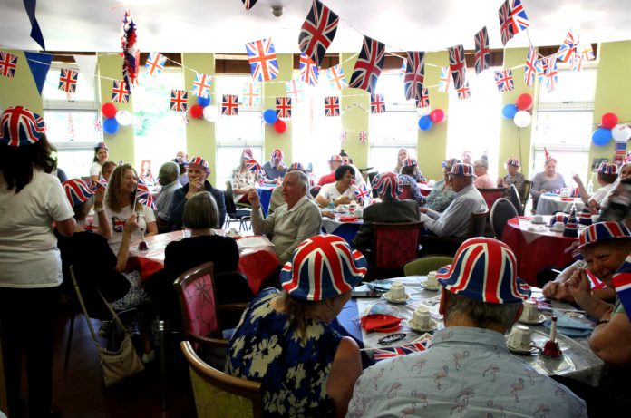 People celebrating the Queen's Platinum Jubilee, wearing hats and with bunting on the ceiling