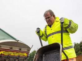 Councillor Steve Reade empties a wheelbarrow of tarmac on to a road