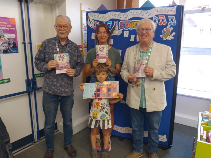 Chair of South Gloucestershire Council, councillor Adrian Rush (right) is joined by a family (centre) and member of staff (left), at Emersons Green Library to mark the launch of the Summer Reading Challenge 2026.